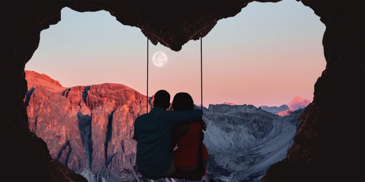 Un couple assis sur une balançoire en forme de cœur, admirant les montagnes au coucher de soleil avec la lune en arrière-plan – voyage de noces romantique en Europe.